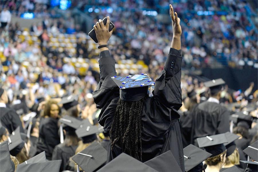 Student raises arms in graduation cap at commencement.